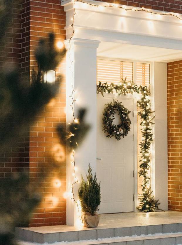 A house entrance at night with a wreath, a lit garland along the doorway and warm string lights.