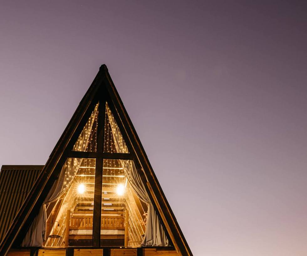 An A-frame cabin glowing with warm light against a twilight sky.